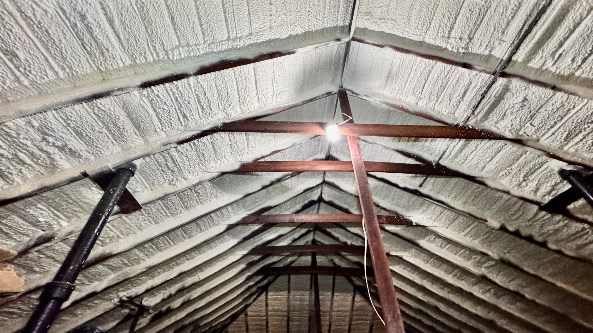 Underside of a New Orleans roof deck fully coated with closed-cell polyurethane foam adhesive, meeting Wind Mitigation requirements even though the original decking is old.