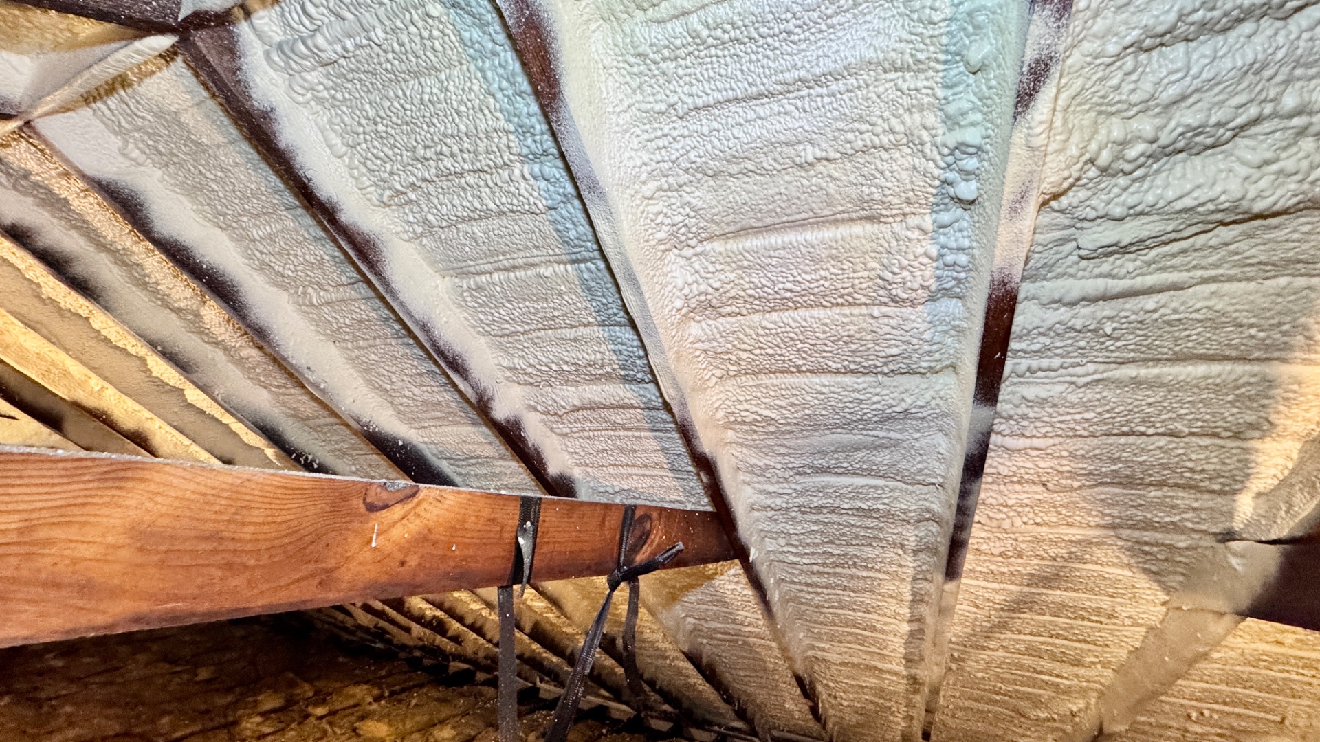 Close-up view of one side of an attic roof deck after closed-cell polyurethane foam adhesive has been applied to every rafter bay.